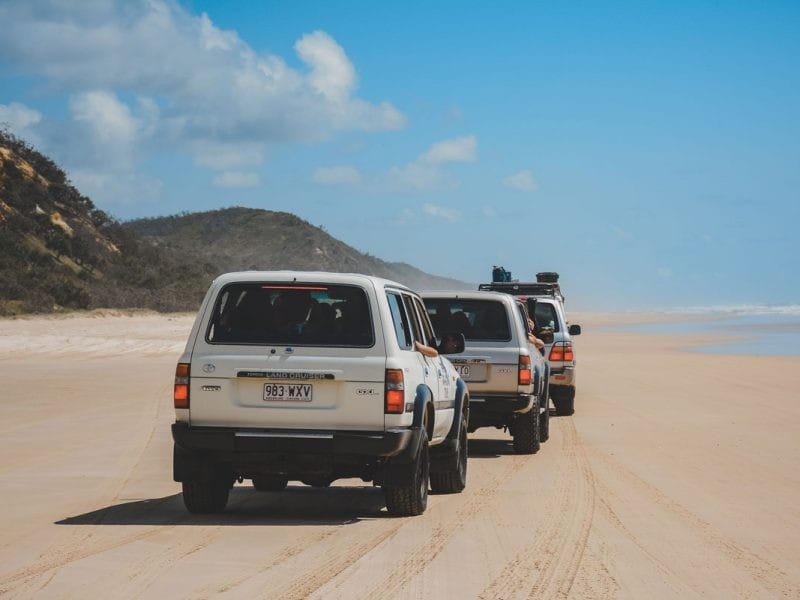 tres coches jeeps por la arena de la playa Fraser Island y el cielo despejado